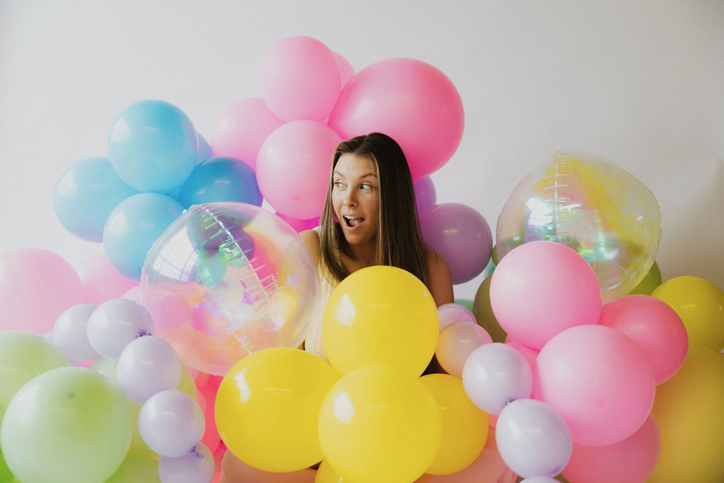 Jenni peeking playfully through a wall of balloons
